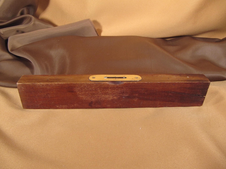 May include: A wooden level with a brass level indicator. The level is brown and has a natural wood finish.