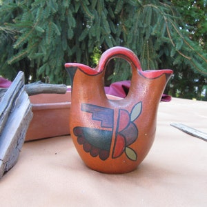 May include: A hand-painted ceramic pitcher with a brown, red and green geometric design. The pitcher has a wide, round base and a narrow spout.