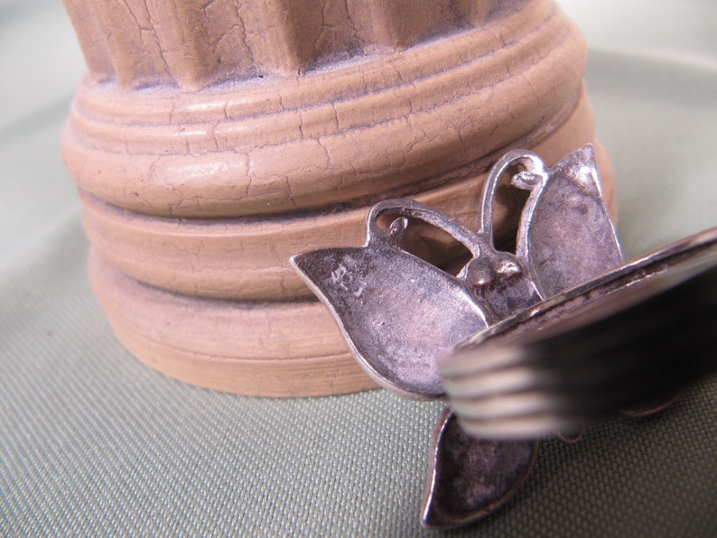 May include: Silver butterfly ring with a textured surface. The ring is in focus and the background is out of focus.