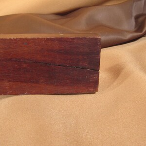 May include: A close-up of a dark brown wooden box with a crack running down the centre. The box is sitting on a light brown surface.