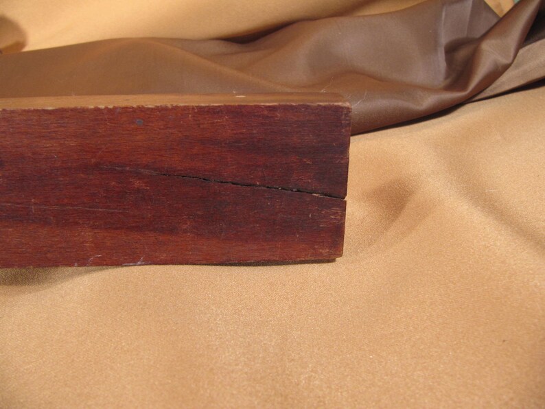 May include: A close-up of a dark brown wooden box with a crack running down the centre. The box is sitting on a light brown surface.