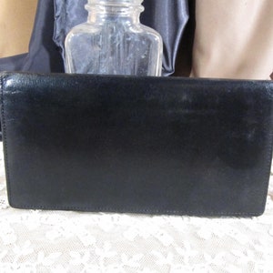 Pode incluir: Uma carteira de couro preta com uma superfície lisa e texturizada. A carteira está fechada e tem uma forma retangular.