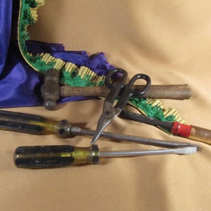 May include: A close-up of a set of tools including a hammer, two screwdrivers, and a pair of scissors. The tools are arranged on a brown surface with a green and yellow fabric in the background.