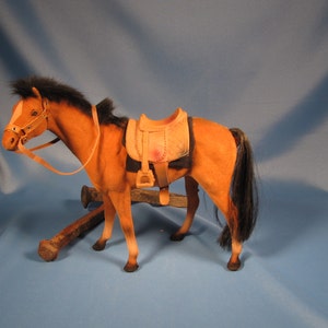 May include: A brown and black toy horse with a saddle and bridle. The horse is standing on a blue surface.
