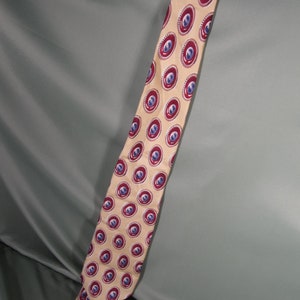 Puede incluir: Una corbata de seda amarilla con un patrón repetido de círculos rojos y azules. Los círculos tienen un contorno blanco y un centro azul con un diseño rojo.