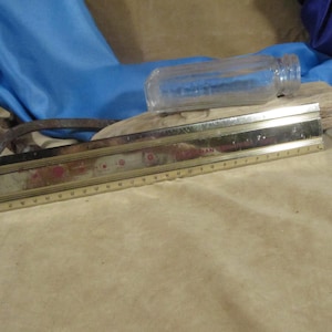 Peut inclure: Une règle en métal doré avec des marques rouges et une bouteille en verre transparent avec une surface texturée. La règle mesure 30,5 cm de long et est graduée en centimètres. La bouteille mesure environ 15 cm de long et a une ouverture ronde.