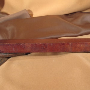 May include: A rectangular, dark red, wooden sharpening stone. The stone is slightly curved on the top and bottom.