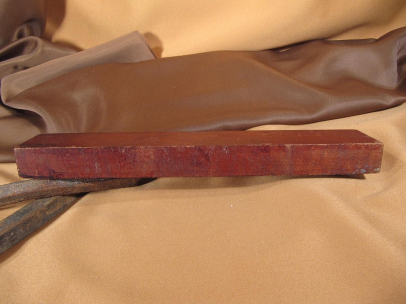 May include: A rectangular, dark red, wooden sharpening stone. The stone is slightly curved on the top and bottom.