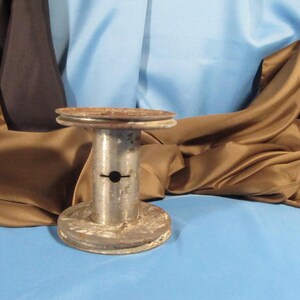May include: A silver metal spool with a hole in the center, sitting on a blue surface. The spool has two metal rings on the top and bottom.