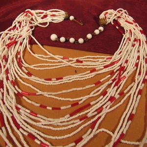 May include: A long white and red beaded necklace with multiple strands. The necklace is made of small, round beads and has a simple design.