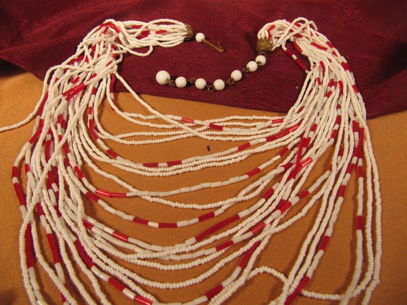 May include: A long white and red beaded necklace with multiple strands. The necklace is made of small, round beads and has a simple design.