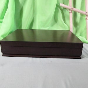 May include: A dark brown wooden box with a hinged lid. The box is closed and sitting on a white surface.