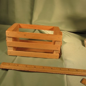 May include: A small wooden crate with three horizontal slats. The crate is made of natural wood and has a light brown color.