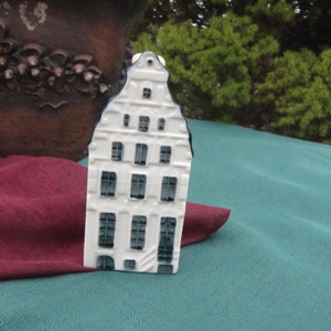 May include: White ceramic miniature house with blue trim and windows. The house has a traditional Dutch design with a steep roof and multiple stories.