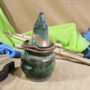 May include: A green and brown ceramic jar with a lid. The jar has a unique, uneven shape and a speckled glaze.
