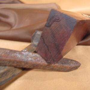 May include: A close-up of a wooden tool with a dark brown finish. The tool has a rectangular shape and a smooth surface. The tool is resting on a brown fabric surface.