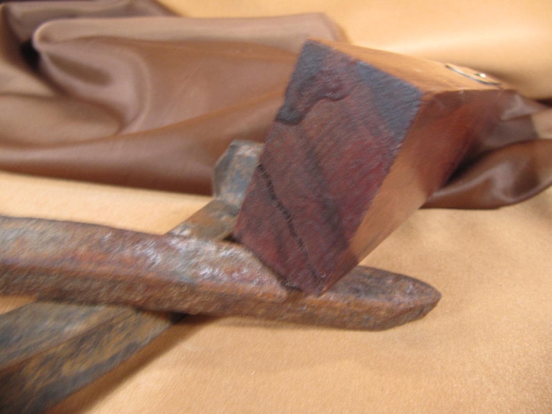 May include: A close-up of a wooden tool with a dark brown finish. The tool has a rectangular shape and a smooth surface. The tool is resting on a brown fabric surface.