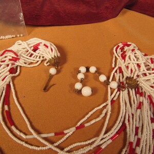 May include: Two strands of white and red beaded necklaces with white bead accents. The necklaces are made of small, round beads and have a tassel-like end.