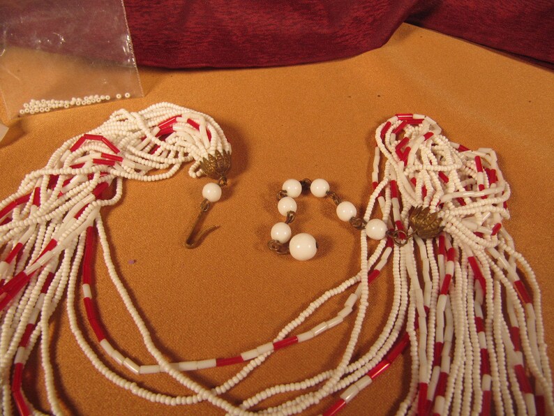 May include: Two strands of white and red beaded necklaces with white bead accents. The necklaces are made of small, round beads and have a tassel-like end.