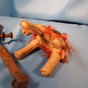 May include: A vintage, hand-stitched, leather toy camel with a brown and orange shaggy mane and tail. The camel is lying on its side with its legs bent. The camel is made of leather and has a stitched seam down the center of its back.