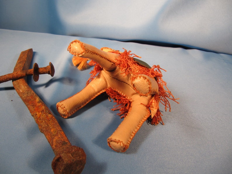 May include: A vintage, hand-stitched, leather toy camel with a brown and orange shaggy mane and tail. The camel is lying on its side with its legs bent. The camel is made of leather and has a stitched seam down the center of its back.