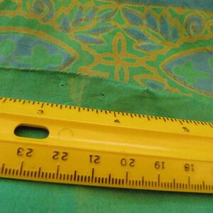 Może przedstawiać: Ż&oacute;łta linijka z czarnymi oznaczeniami, mierząca do 60 cm, leży na zielonym materiale z kwiatowym wzorem.