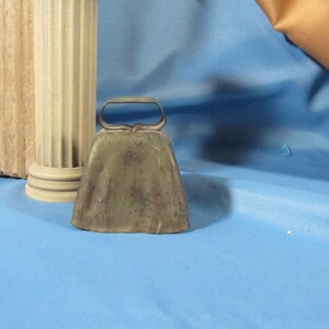 May include: A green metal cowbell with a tarnished finish and a simple, rounded handle.