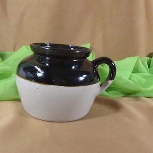 Puede incluir: Una olla de frijoles de cerámica esmaltada marrón y blanca con una sola asa.