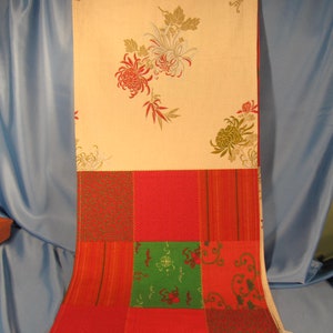 May include: A cream-colored fabric table runner with a floral pattern. The runner is made of patchwork fabric with red, green, and cream-colored squares.
