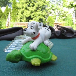 Może przedstawiać: Figurki dalmatyńczyka w kolorze białym i czarnym, jadącego na figurce zielonej żółwia. Żółw ma brązowy pancerz z zielonym spodem.