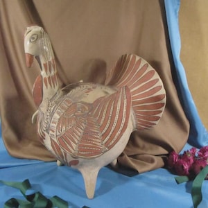 May include: A ceramic turkey figurine with a cream-colored body and red-brown wing and tail details. The turkey has a long neck and a beak. The figurine is on a blue surface with a brown and blue backdrop.