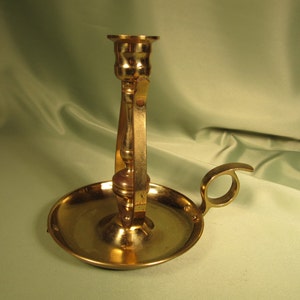 May include: A gold metal candle holder with a round base and a handle. The candle holder has a decorative design and is perfect for adding a touch of elegance to any room.