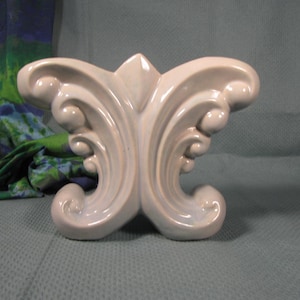 May include: A light gray ceramic sculpture in the shape of a butterfly with intricate details. The sculpture has a smooth, glossy finish.