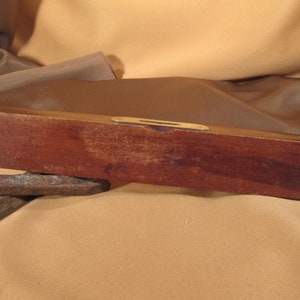 May include: A wooden level with a brass spirit level. The level is brown and has a slight crack on the top.