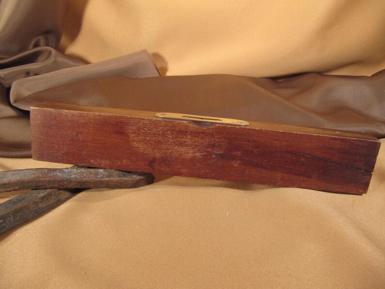 May include: A wooden level with a brass spirit level. The level is brown and has a slight crack on the top.