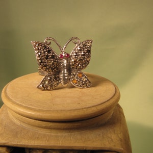 May include: A silver butterfly ring with marcasite and red and yellow gemstones.