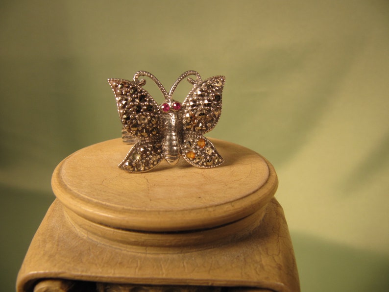 May include: A silver butterfly ring with marcasite and red and yellow gemstones.