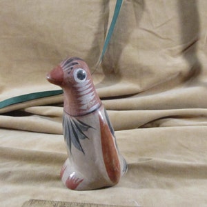 Puede incluir: Una figurita de pájaro de cerámica pintada a mano con detalles en marrón, blanco y negro. El pájaro tiene un pico largo y un cuerpo redondo.