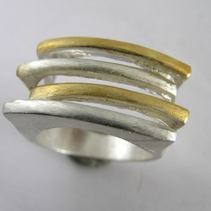 May include: A silver ring with three gold bands, each band is a different width. The ring is made of metal and has a smooth finish.