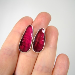 Könnte beinhalten: Ein Paar Ohrringe mit einer silbernen Fassung und einem tiefrosa, tropfenförmigen Glasstein.