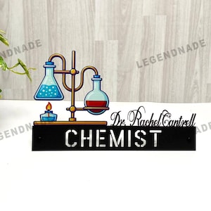 Può includere: Un cartello in metallo nero con la scritta "CHEMIST" in bianco, raffigurante un'attrezzatura da laboratorio stilizzata con becher e un bruciatore. Il cartello include anche il nome "Dr. Rachel Cantrell".
