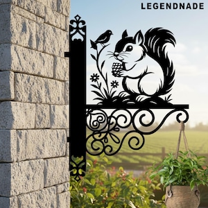 May include: Black metal squirrel and bird hanging sign with the text "LEGENDNADE". The sign features a squirrel holding a pinecone, with a bird perched on a branch. A hanging basket with greenery is below.