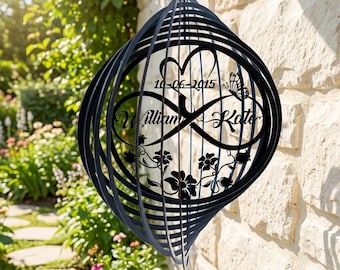 May include: A black metal wind spinner featuring a spherical cage design. The center displays an infinity symbol, a heart, a butterfly, and floral motifs. The text reads "William", "Kate", and the date "10-06-2015" in a script font.