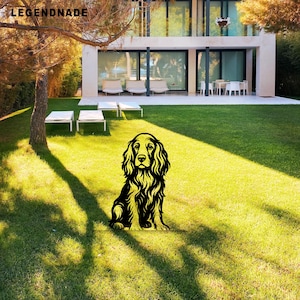 Könnte beinhalten: Schwarze und gelbe Metall-Silhouette eines Cocker Spaniel-Hundes auf einem grünen Rasen vor einem modernen Haus. Der Hund hat detailliertes Fell und Gesichtszüge. Das Wort "LEGENDNADE" ist oben links zu sehen.