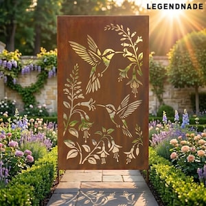 Puede incluir: Una pantalla de jardín rectangular de metal envejecido con diseños recortados de colibríes y elementos florales. La pantalla es marrón con un tono dorado, ubicada en un jardín con exuberante vegetación y flores. El texto "LEGENDNADE" es visible en la parte superior.