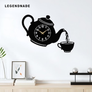 May include: Black wall clock in the shape of a teapot pouring into a teacup. The clock face is white with black numbers and gold hands. The brand name "LEGENDNADE" is printed at the top left.