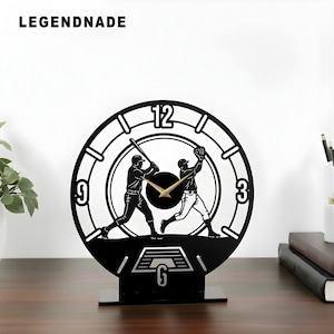 May include: Black baseball-themed clock with a silhouette design of two players. The clock face features the numbers 3, 6, 9, and 12, with gold-colored clock hands. The clock is on a black stand and the brand name "LEGENDNADE" is at the top.