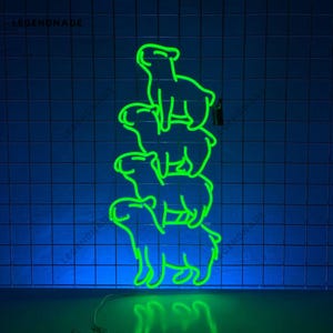 Könnte beinhalten: Ein Neon-Schild mit vier grünen Umriss-Hunden, die übereinander gestapelt sind. Die Hunde sind in Pyramidenform angeordnet, wobei der unterste Hund auf dem Boden steht. Das Schild ist an einer blauen gekachelten Wand befestigt.