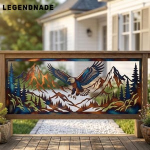 May include: A rectangular metal wall art panel featuring a laser-cut design of a bald eagle in flight over a mountain range with pine trees. The metal has a multi-colored finish with blue and copper tones. The text LEGENDNADE is visible.