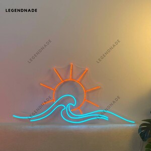 Puede incluir: Un letrero de neón que representa un sol naranja estilizado poniéndose detrás de una ola azul. El letrero está montado en una pared blanca.